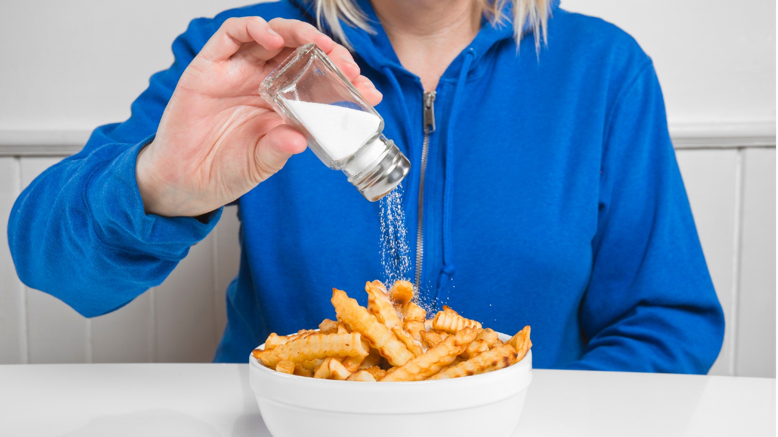 Photo of woman adding salt to a bowl of hot chips